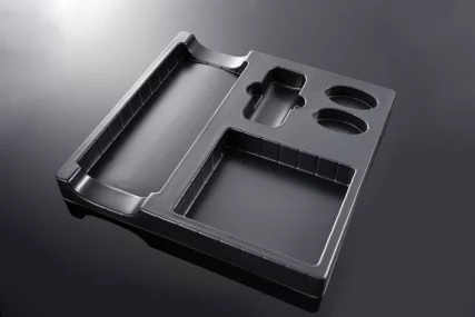Black thermoformed plastic tray with multiple compartments and oval slots on a dark background.