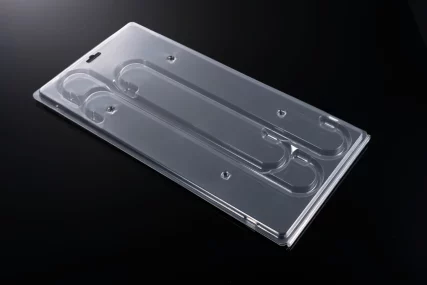 Clear plastic blister pack tray with molded compartments and hang hole on black background.