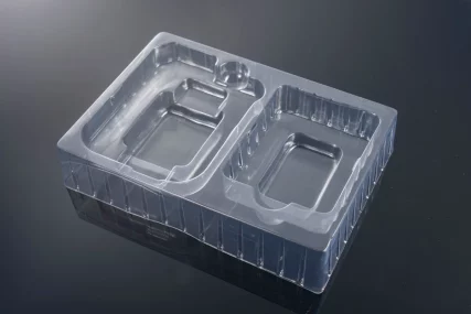 Clear plastic thermoformed tray with two rectangular and one round compartment on a dark background.