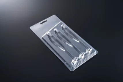 Clear plastic blister pack with molded cavities for two elongated items, resting on a dark reflective surface.